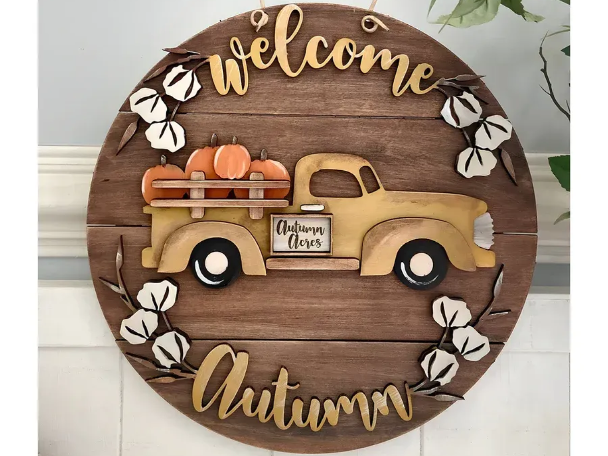 Wooden fall-themed door sign with a yellow truck carrying pumpkins, cotton accents, and