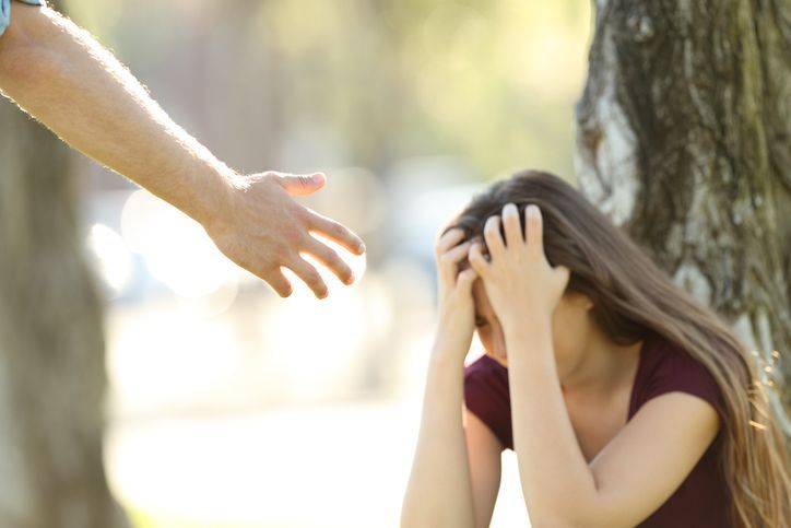 A man is reaching out to help a woman who is covering her face with her hands.