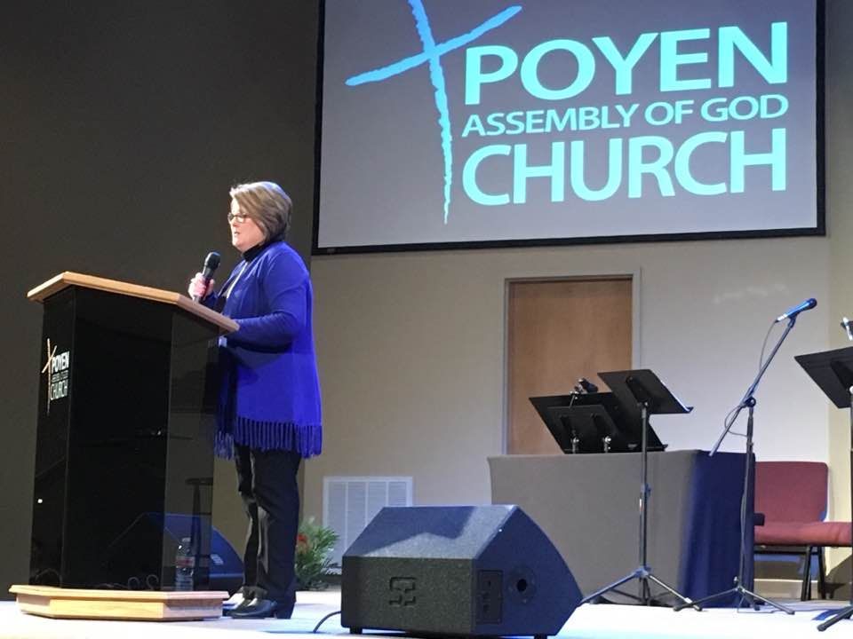 Rhonda Johnson speaking at a podium in front of a POYEN Assembly of God Church.