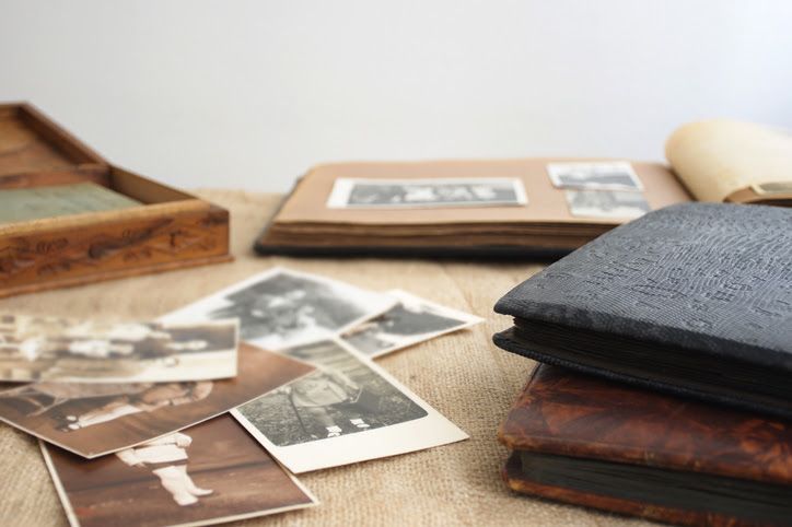 Photo albums are stacked with photos scattered on a table.
