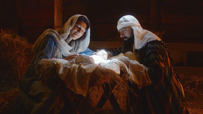 Mary and Joseph gaze at the newborn baby Jesus in a wooden manger, lit by soft light.