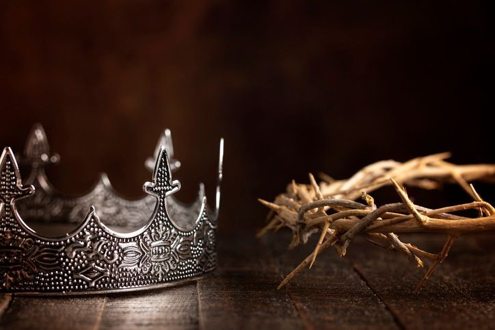 Silver crown and a crown of thorns on a wooden surface.