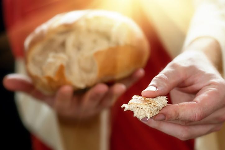 A piece of bread is in a person's left hand, with the loaf of bread in their right hand.