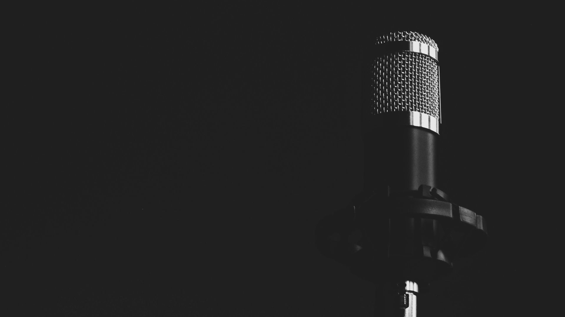 Black and white photo of a vintage microphone. Dark background, microphone in the center, top lit.