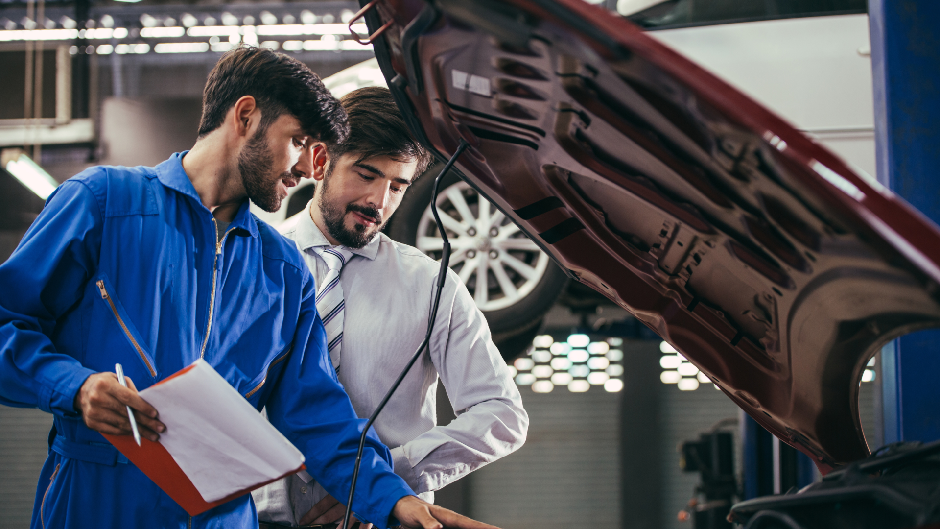 Mechanic in blue coveralls and businessman looking at engine in a garage.