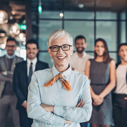 Business team, senior woman in front smiling with arms crossed.