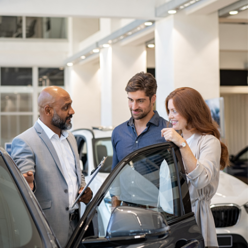 A car salesperson showing a car to a smiling couple in a dealership.