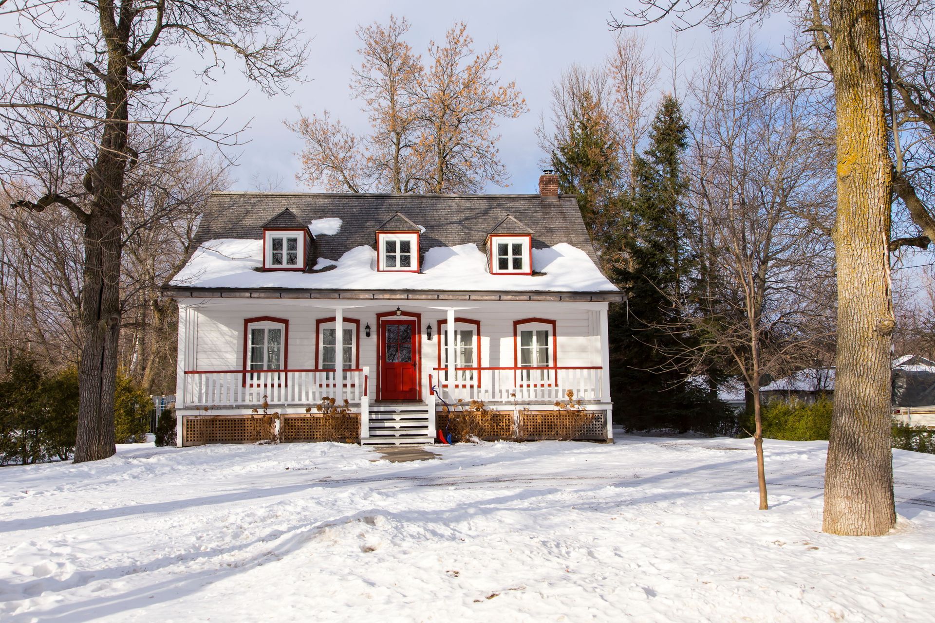 Une maison blanche avec une porte rouge est recouverte de neige