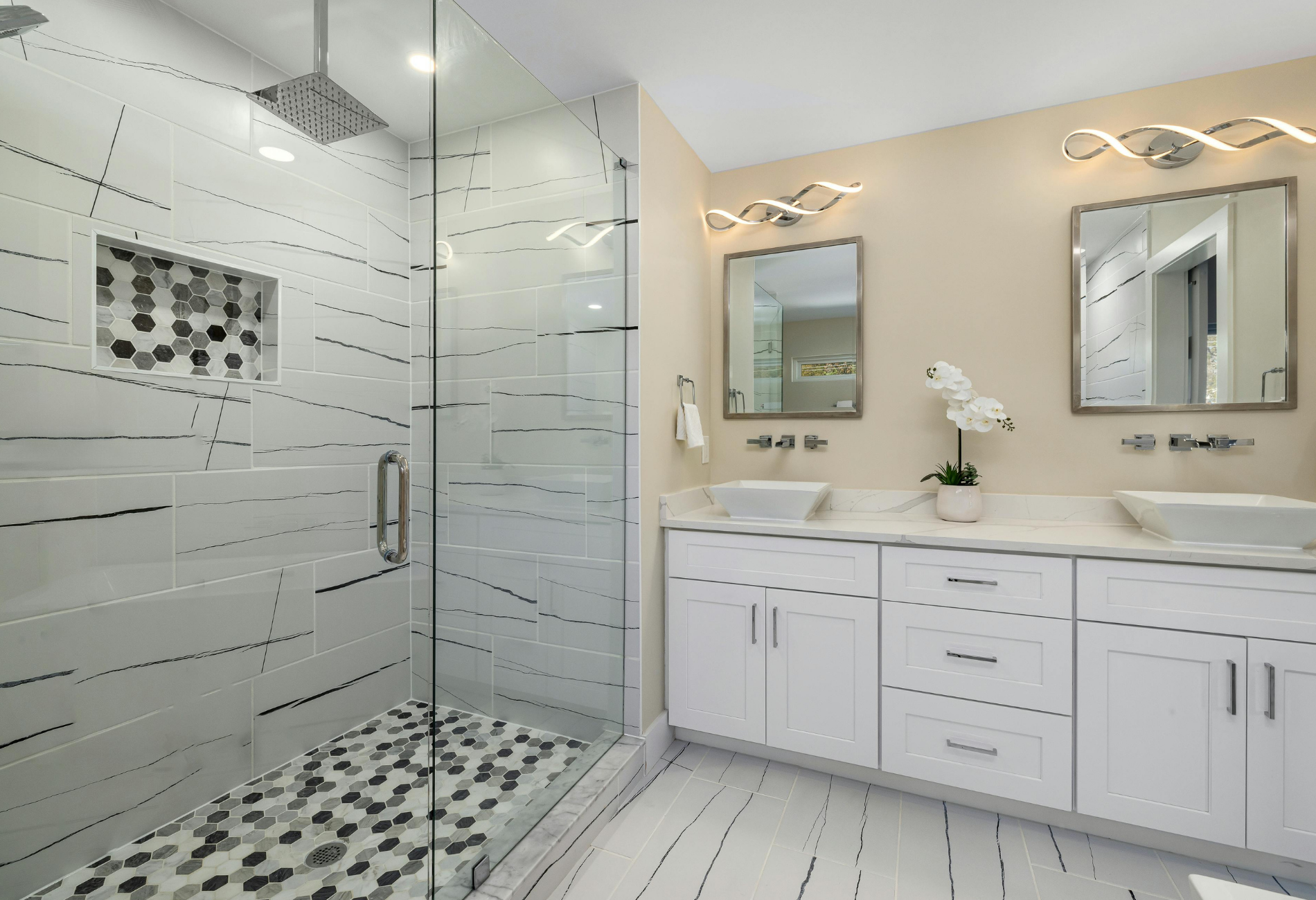 Modern bathroom with shower, dual sinks, and white cabinets. Gray, white, and tan color scheme.