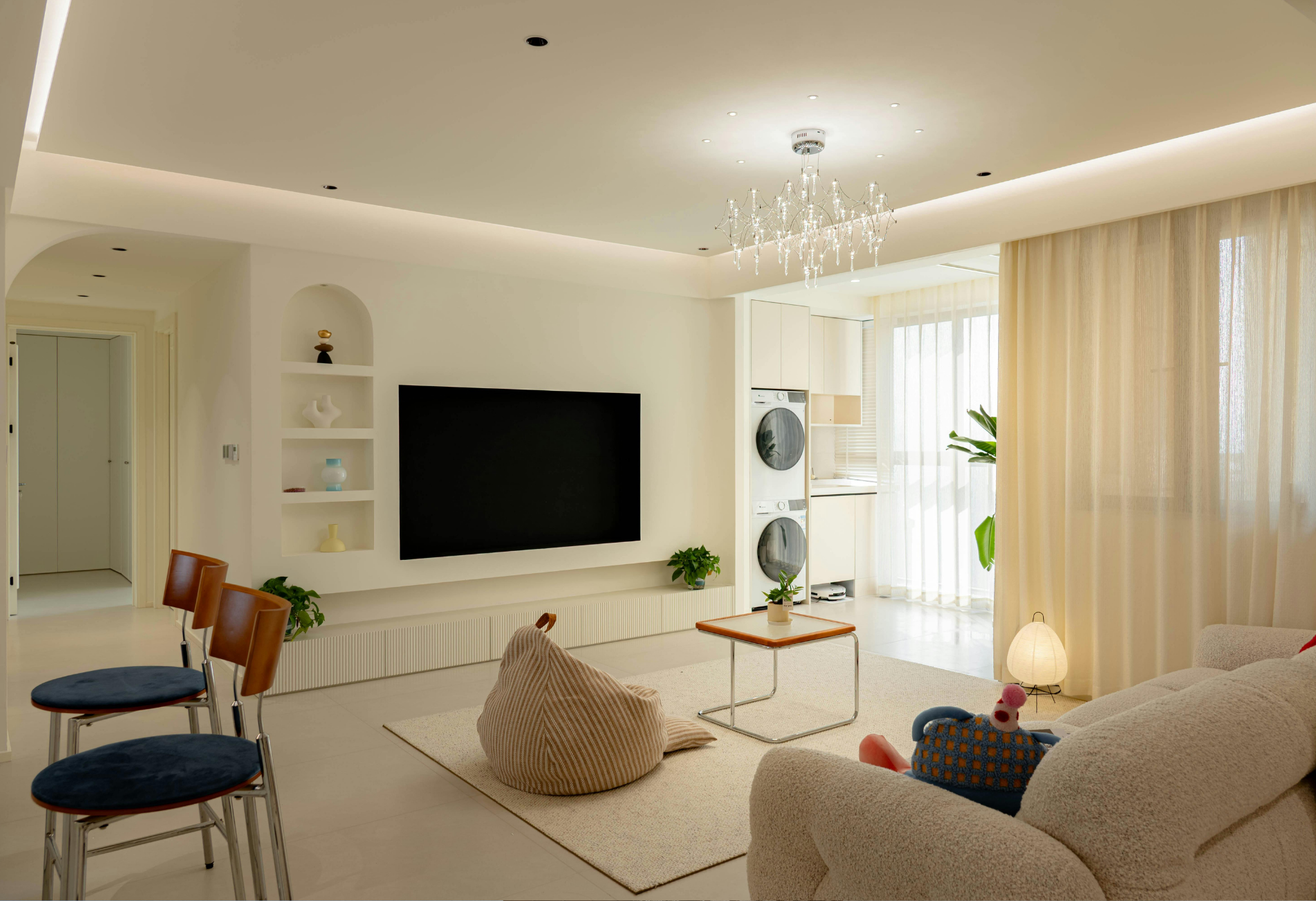 Living room with white walls, built-in shelving, TV, and cream curtains.