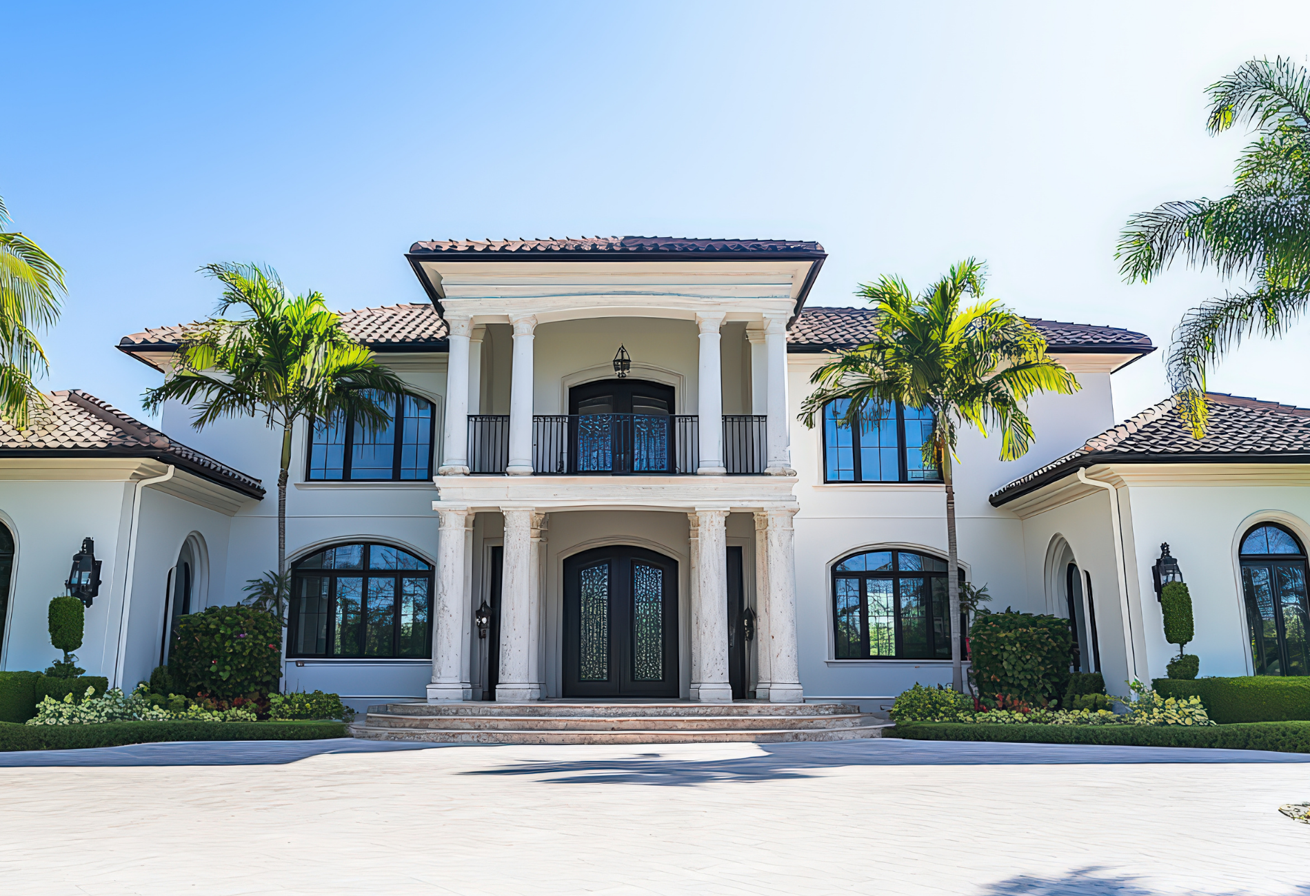 White luxury home with columns, balcony, and palm trees.