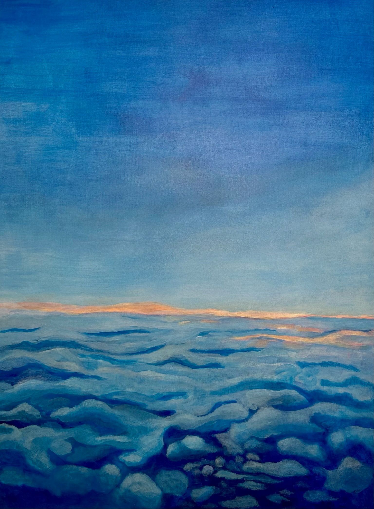 Blue sky over a sea of clouds with a faint orange horizon at sunrise.