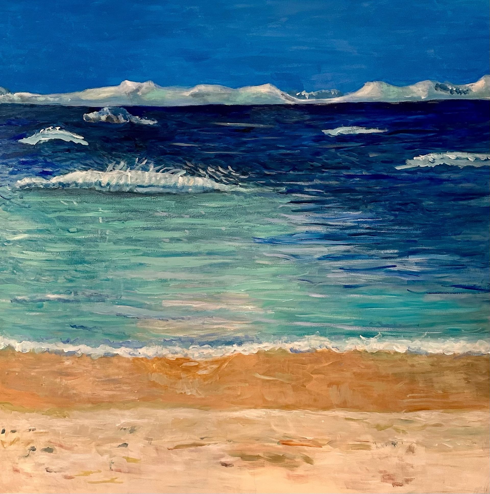 Blue ocean waves with a sandy beach and distant white clouds under a clear sky