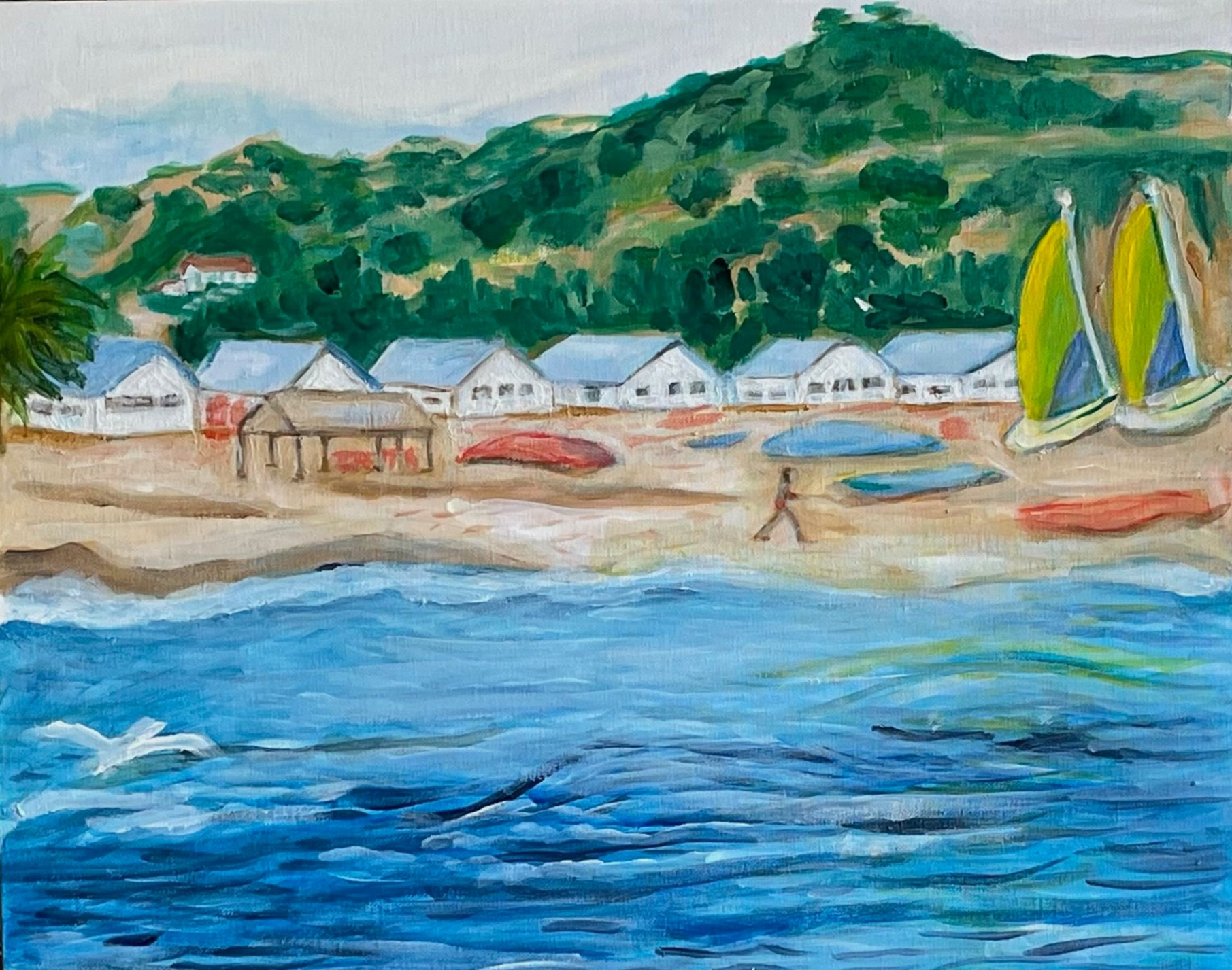 Waterfront village with white houses, sailboats, green hills, and blue water in the foreground