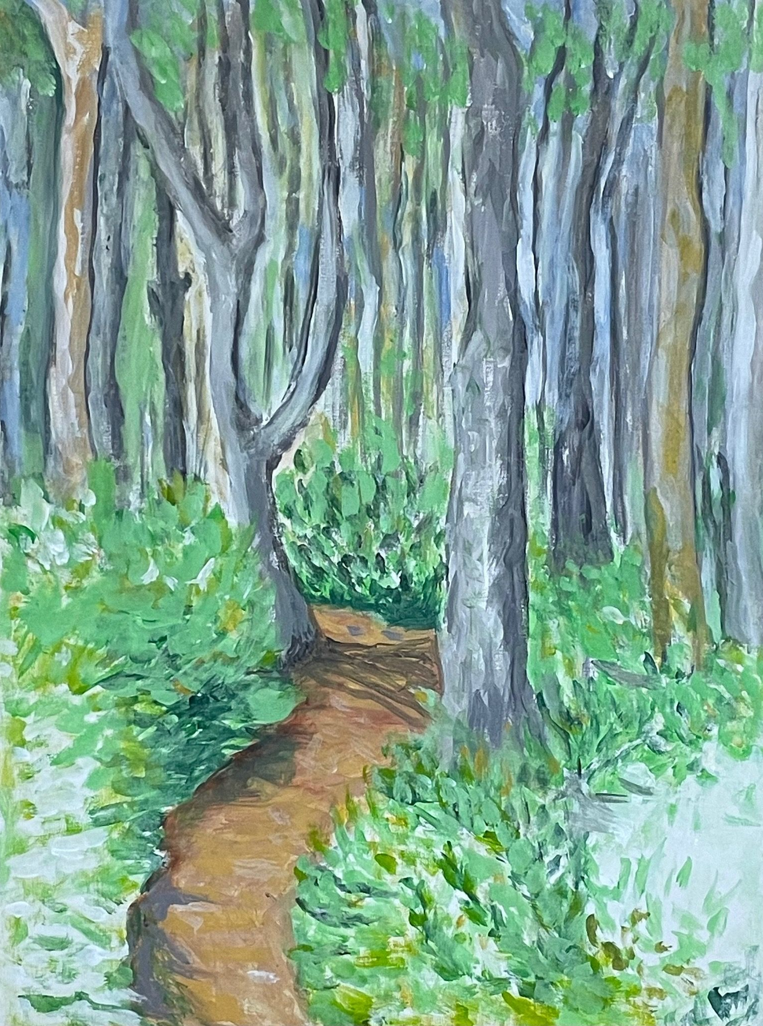 A winding brown trail through a lush green forest with tall gray trees.
