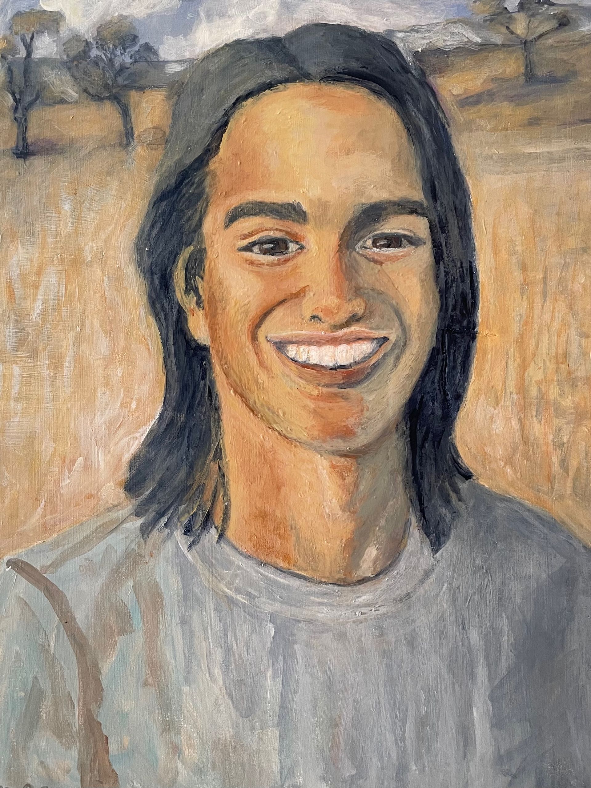 Smiling person with shoulder-length dark hair in a gray shirt against a soft outdoor landscape background