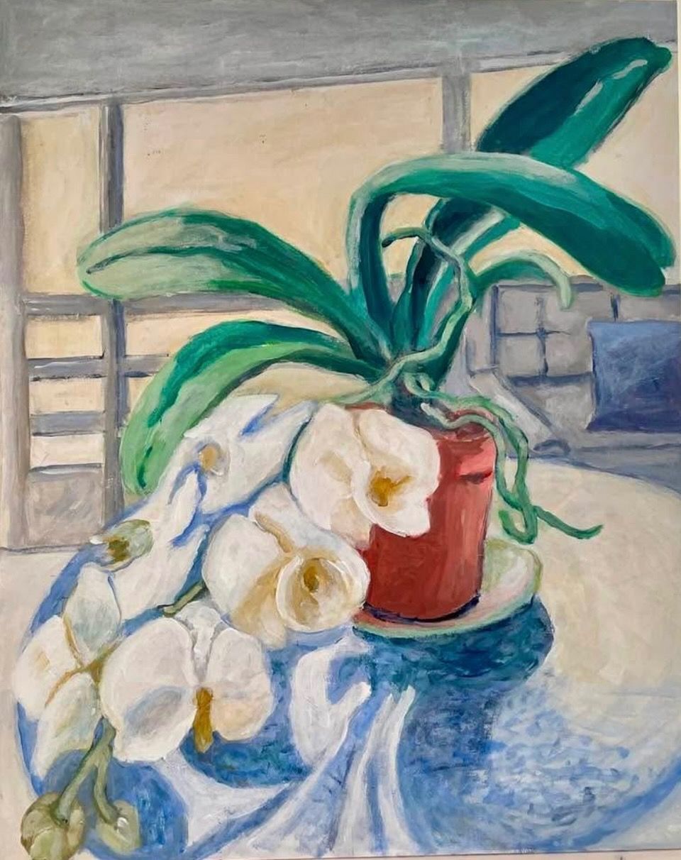 White flowers in a red vase with broad green leaves on a blue cloth by a window