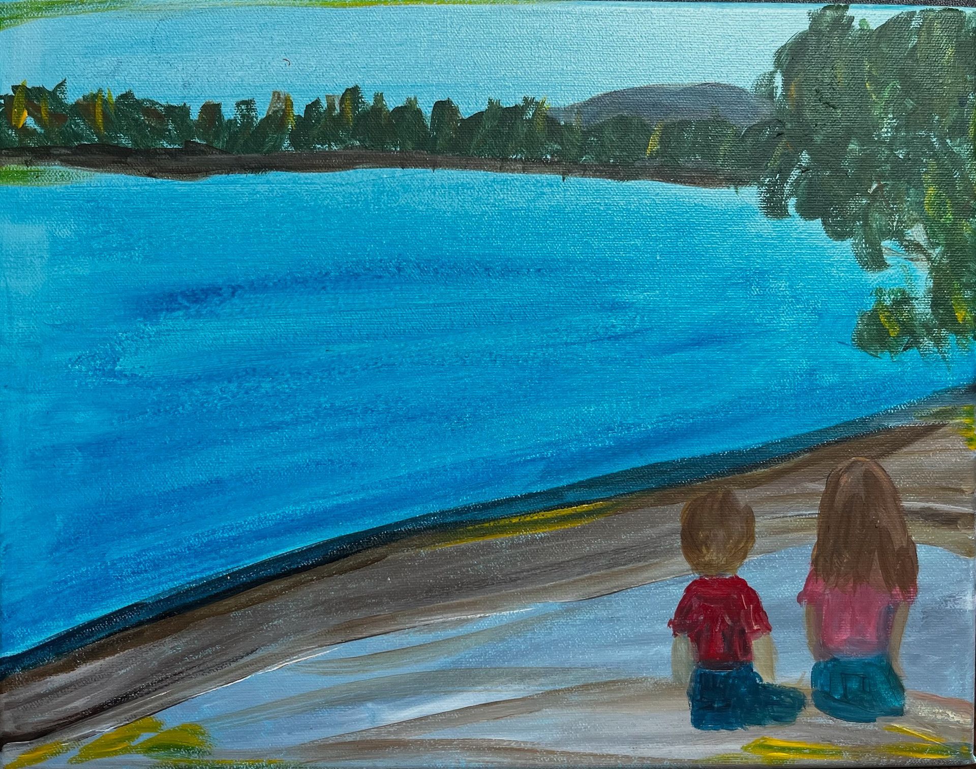 Two children sit by a blue lake, looking across the water from a shaded shore.