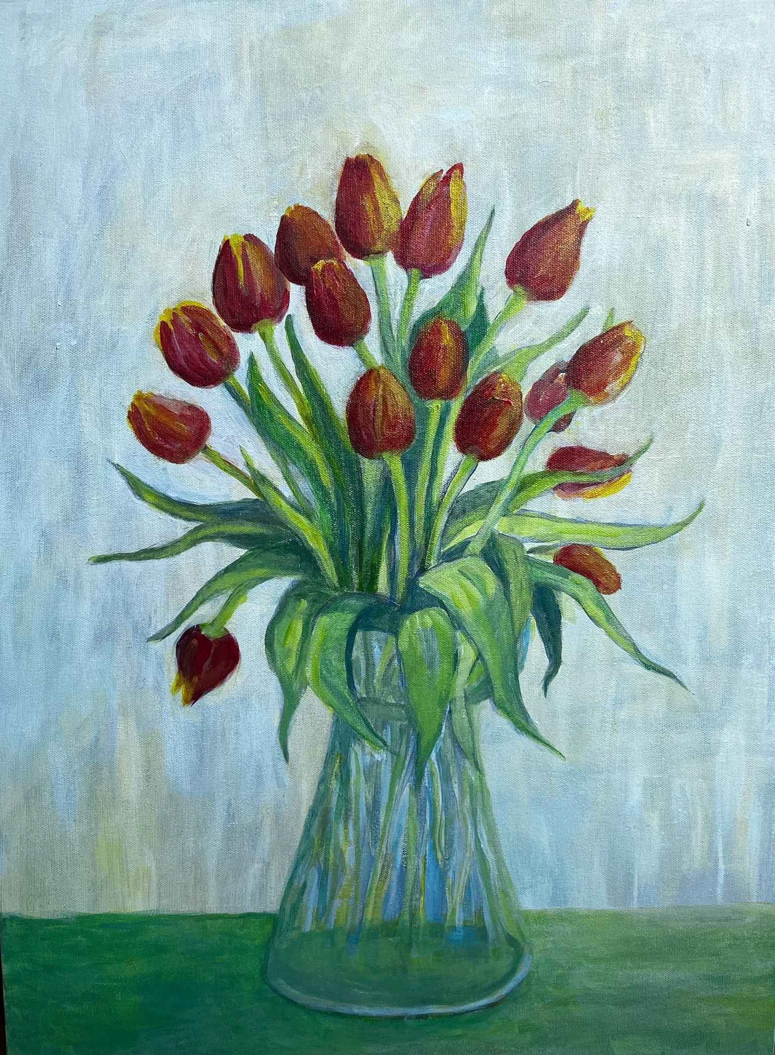 A vase of red tulips and green leaves on a blue-green background