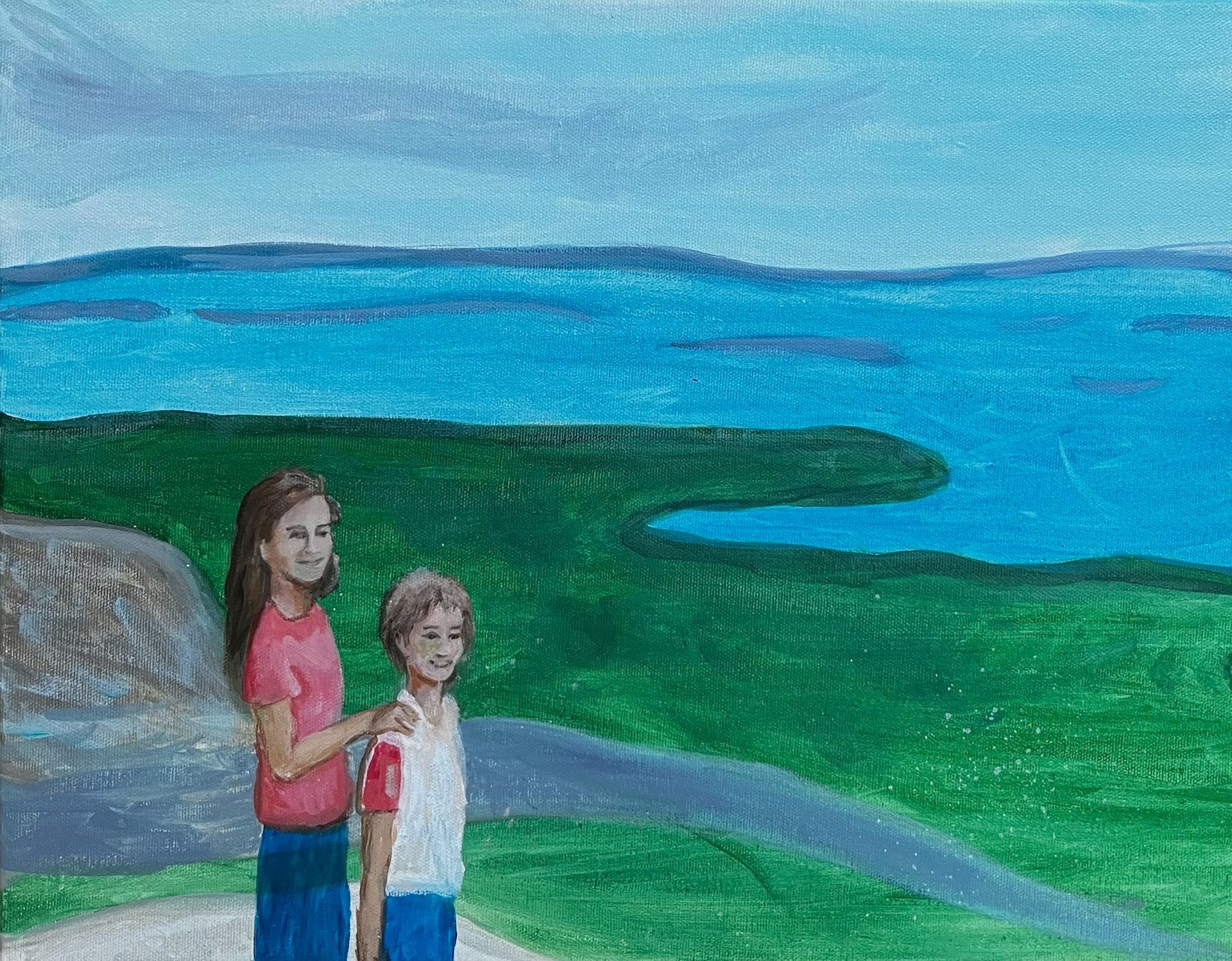 Two children stand by a rocky shore with green land and blue water under a cloudy sky.