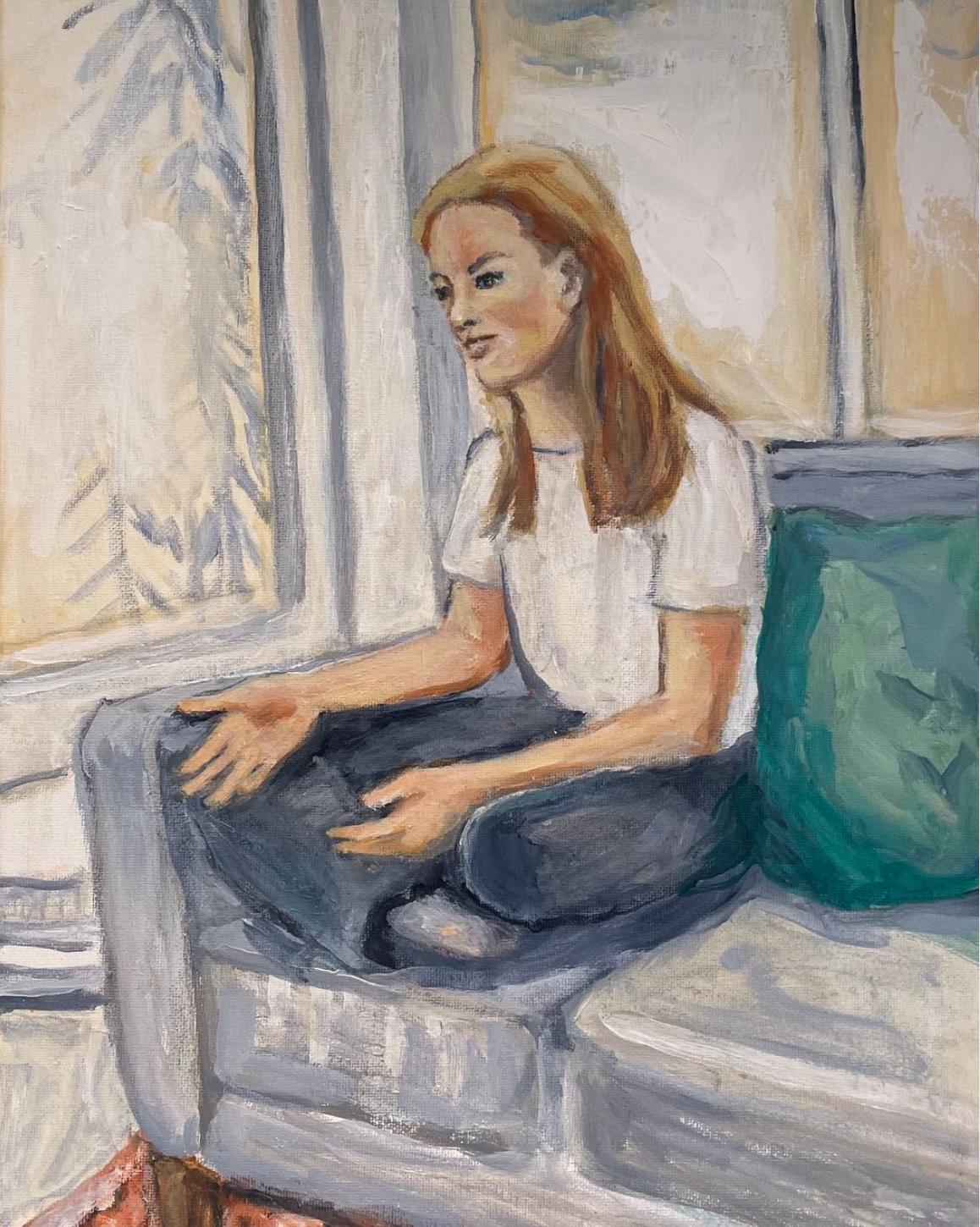 Person sitting cross-legged on a couch by a window, with a teal pillow beside them.