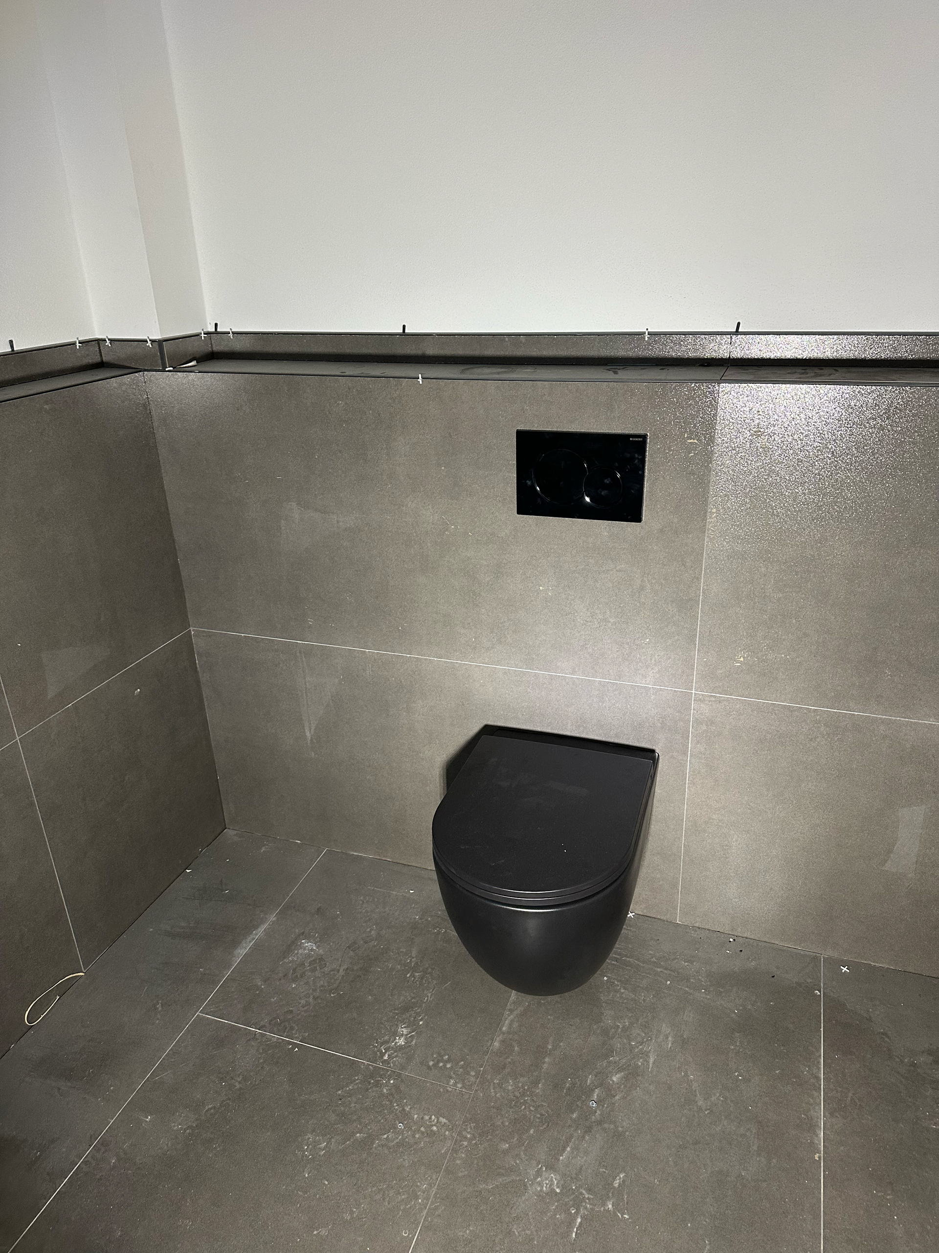 Eine schwarze Toilette steht auf einem gefliesten Boden in einem Badezimmer.