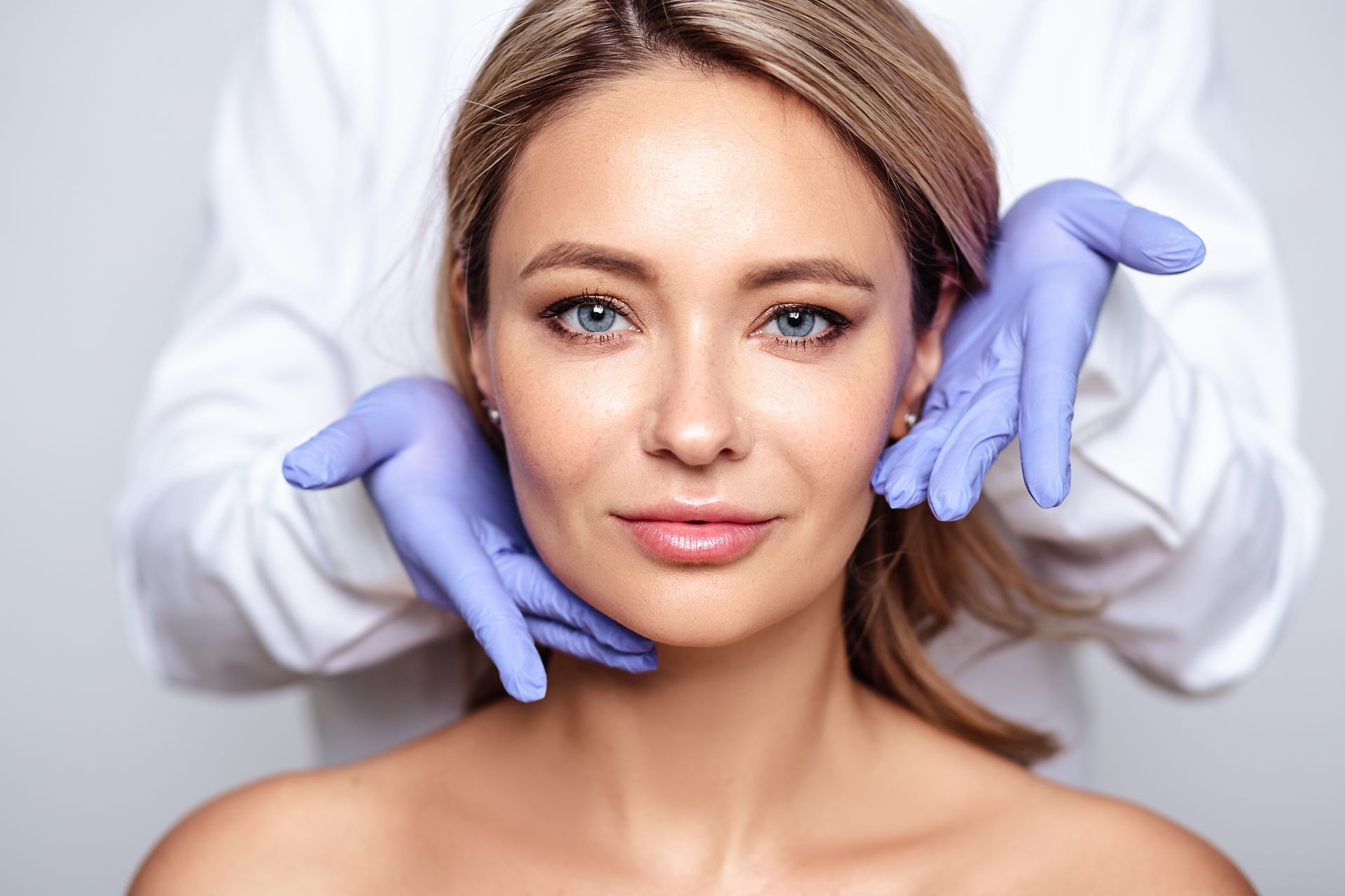 A woman's face is examined by gloved hands.