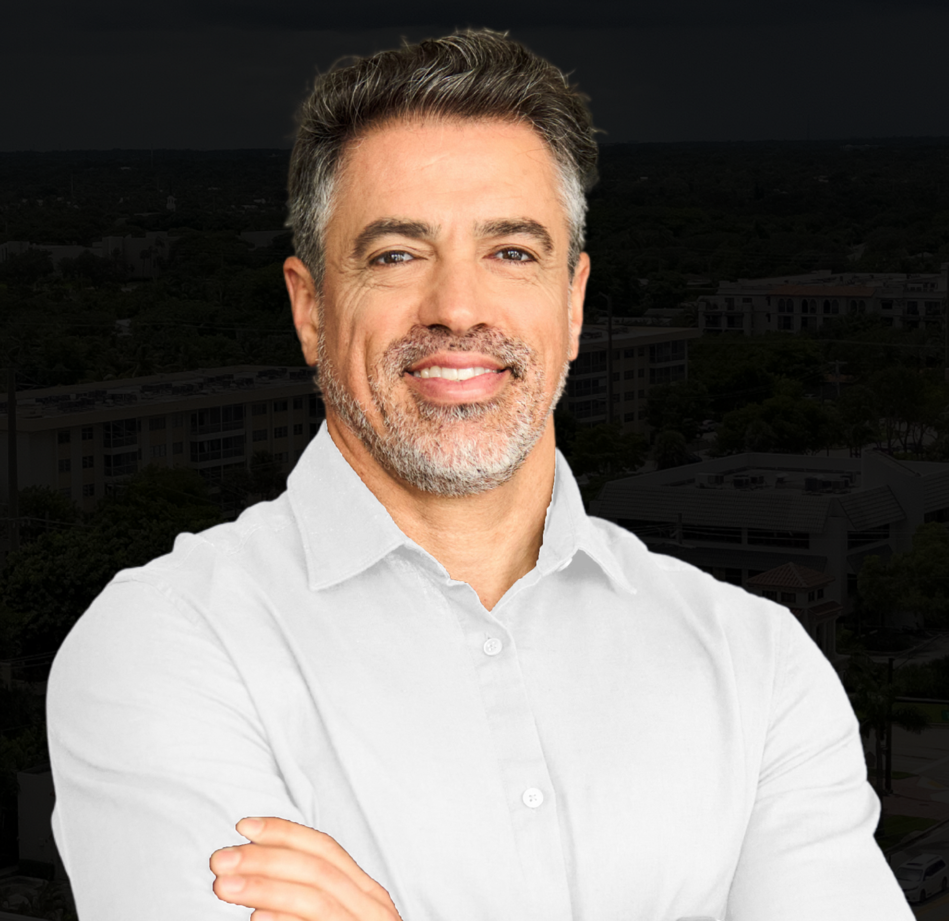 A man with a beard is wearing a white shirt and smiling with his arms crossed.