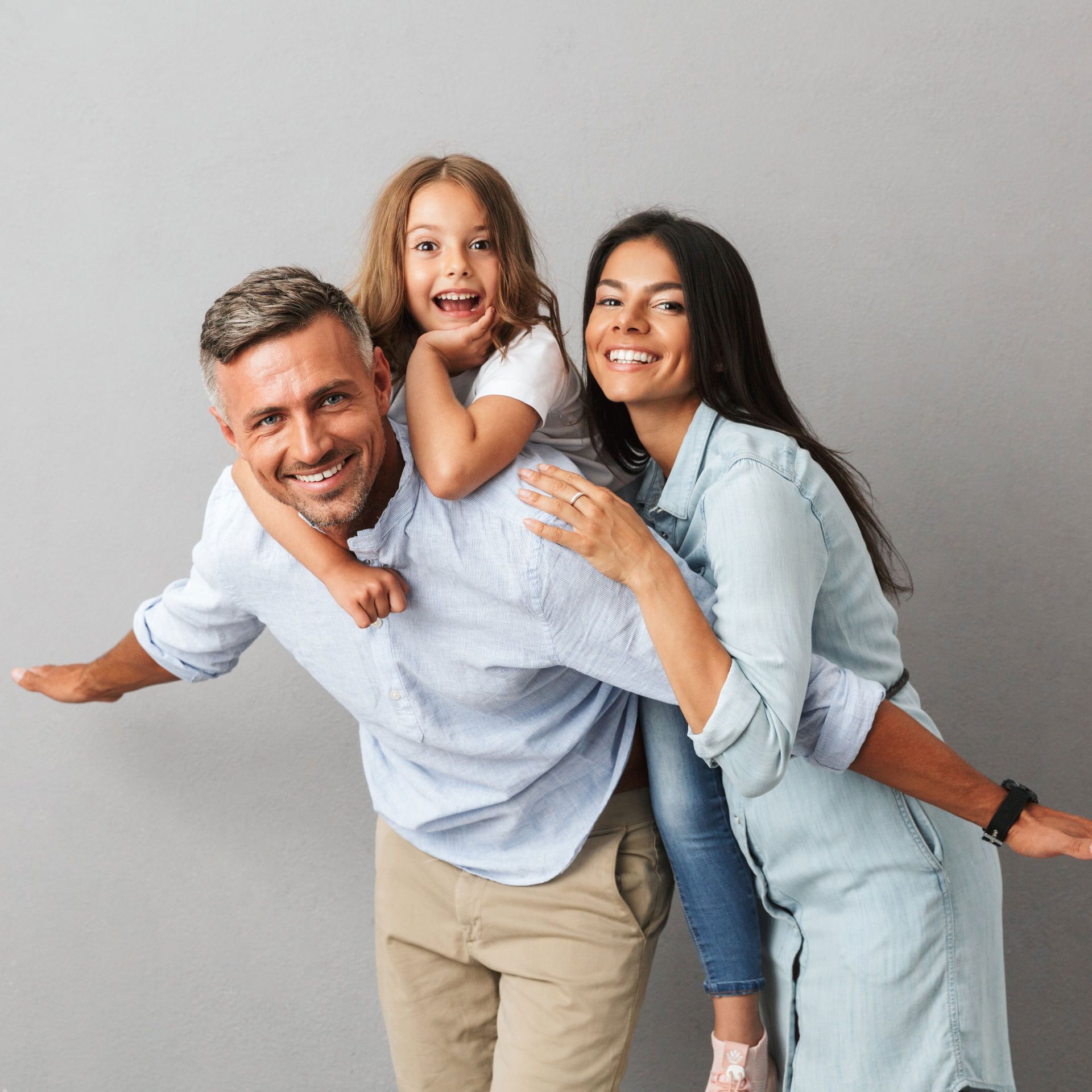 A man and woman are giving a little girl a piggyback ride