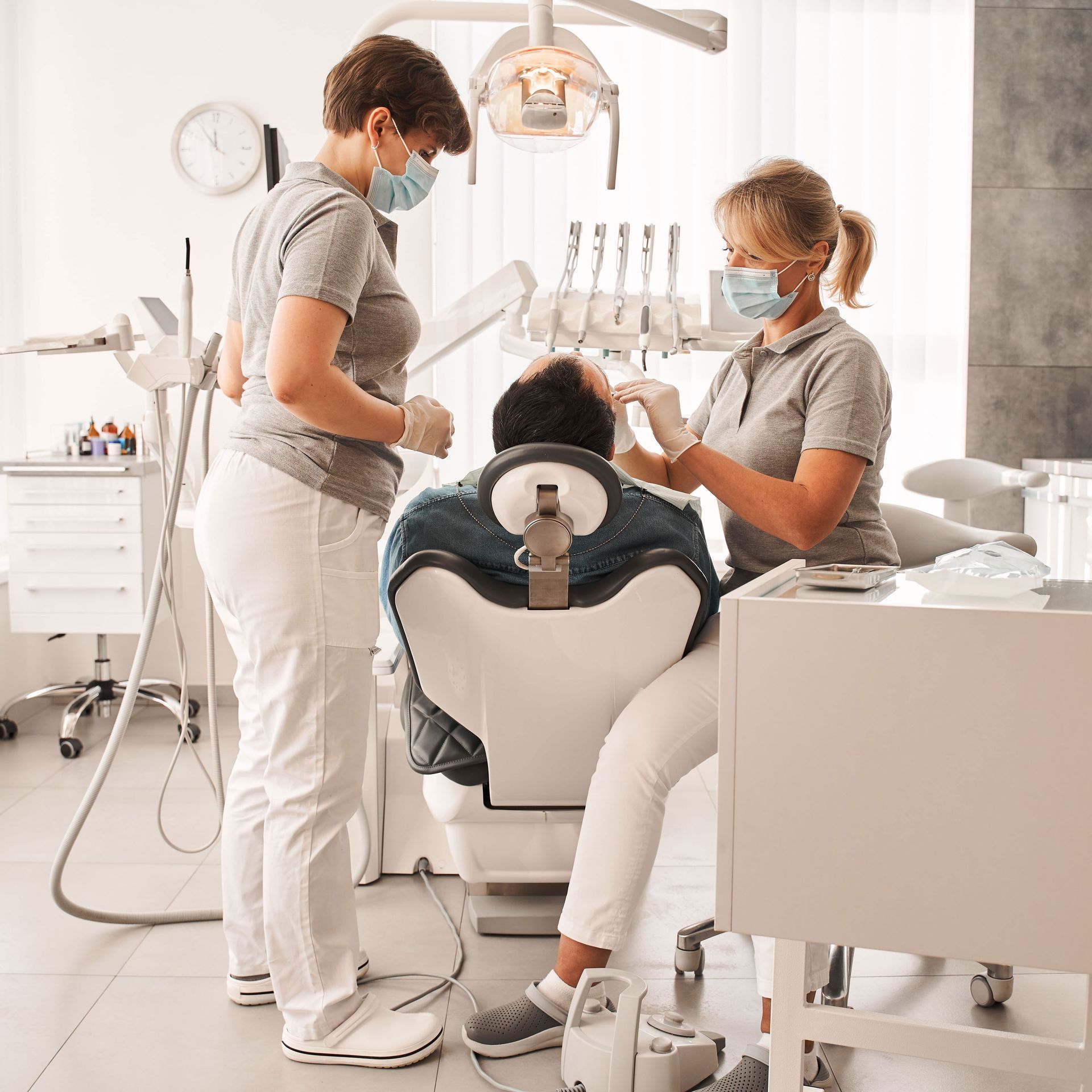 Two female dentists are working on a patient in a dental office.