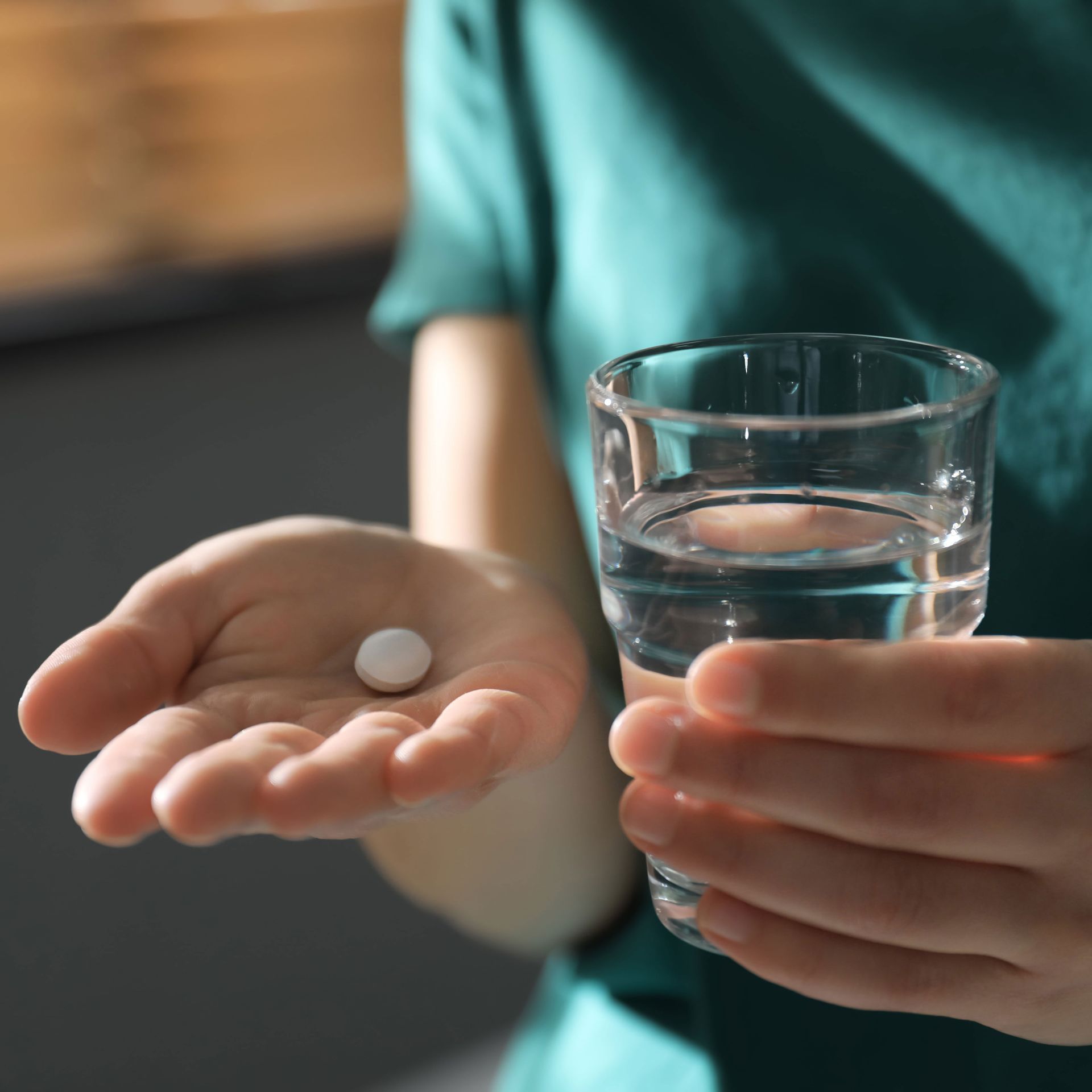 A person is holding a glass of water and a pill in their hand