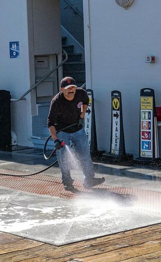 A man is cleaning a wooden floor with a high pressure washer.