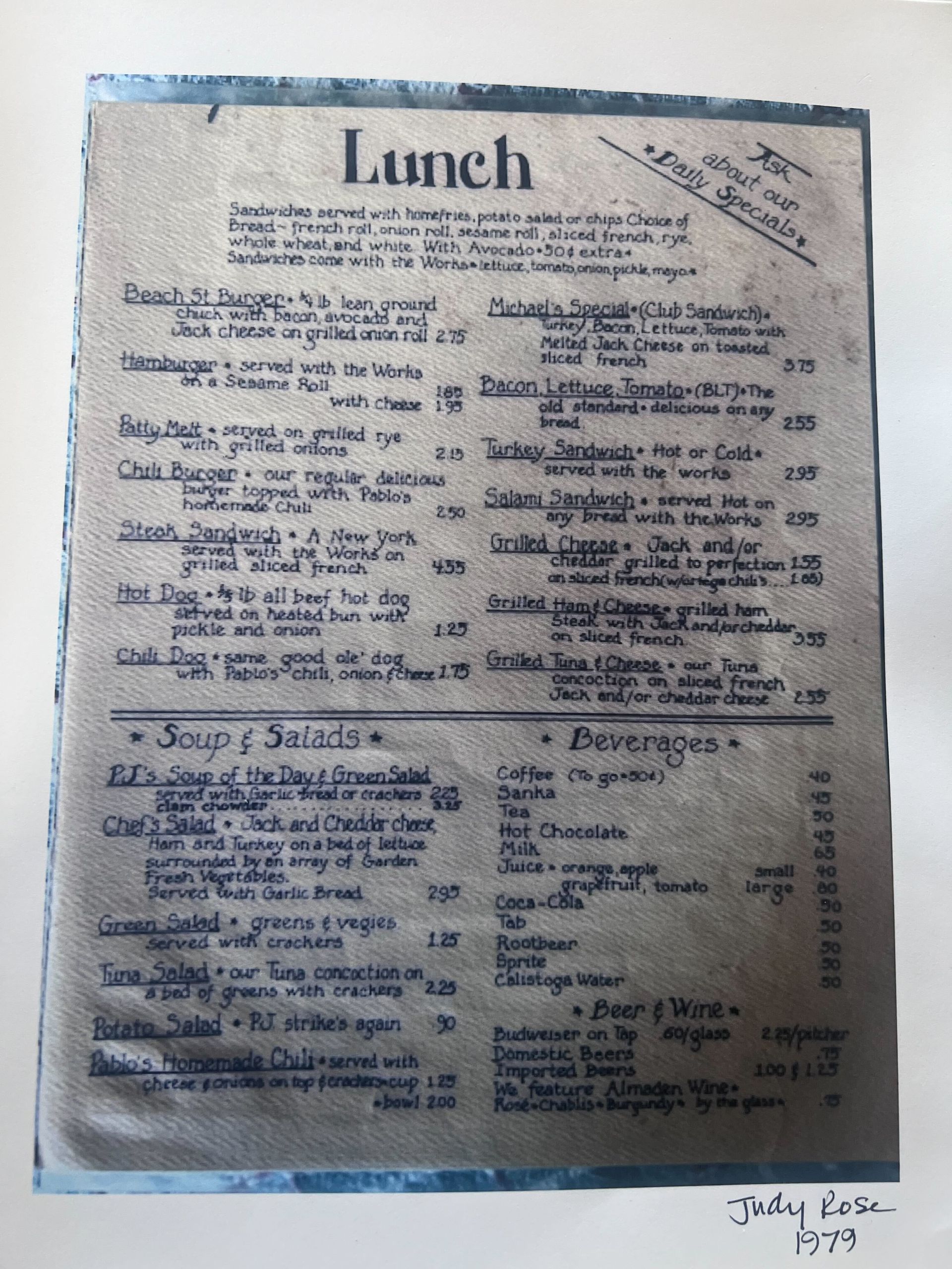 Blurry photo of a printed lunch menu on white paper with a blue border, hanging on a wall.