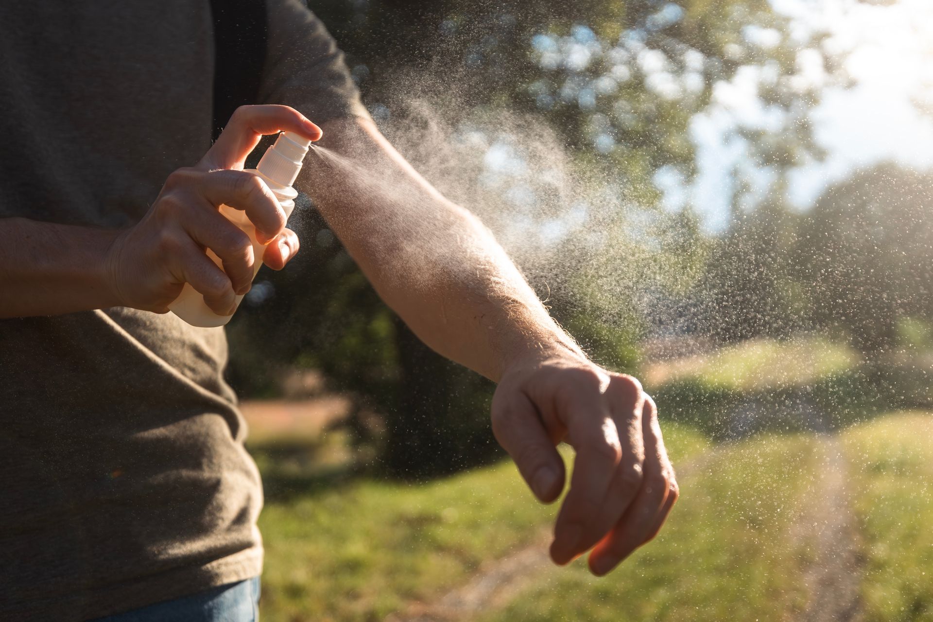 Person spraying insect repellent on arm outdoors