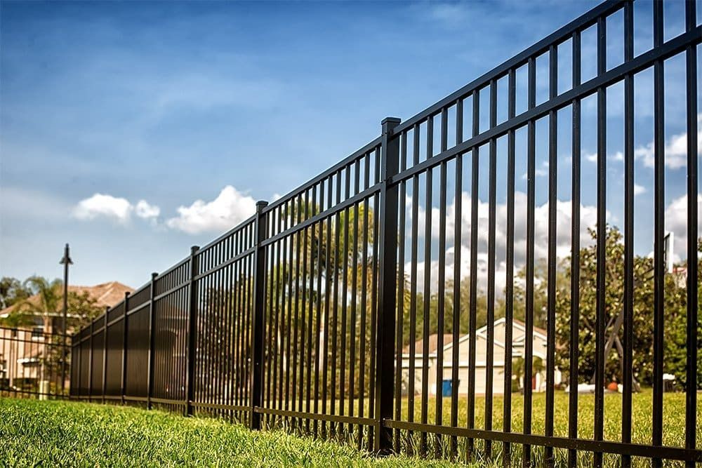 Black metal fence on green grass against a blue sky with clouds.