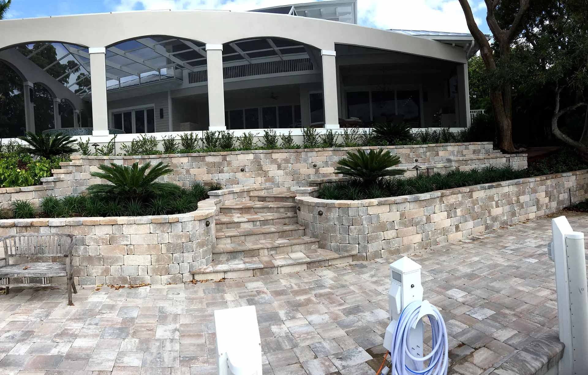 Stone steps lead up to a tiered landscape with a house featuring a white porch and pillars