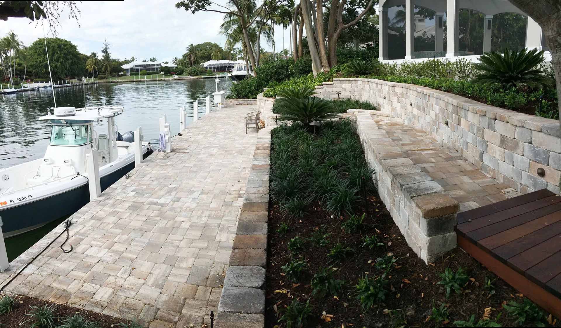 Dock with a boat, stone pathway and retaining wall with greenery, next to water