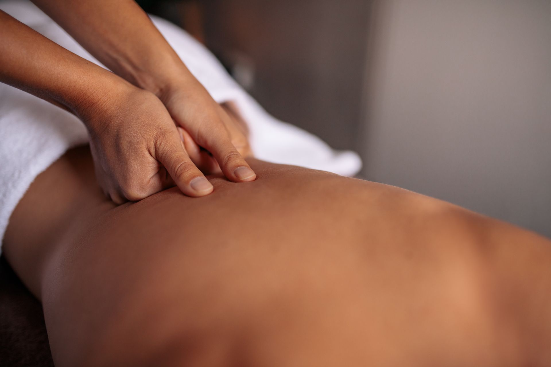 Hands massaging a person's back, focusing on the lower back area. White towel present.