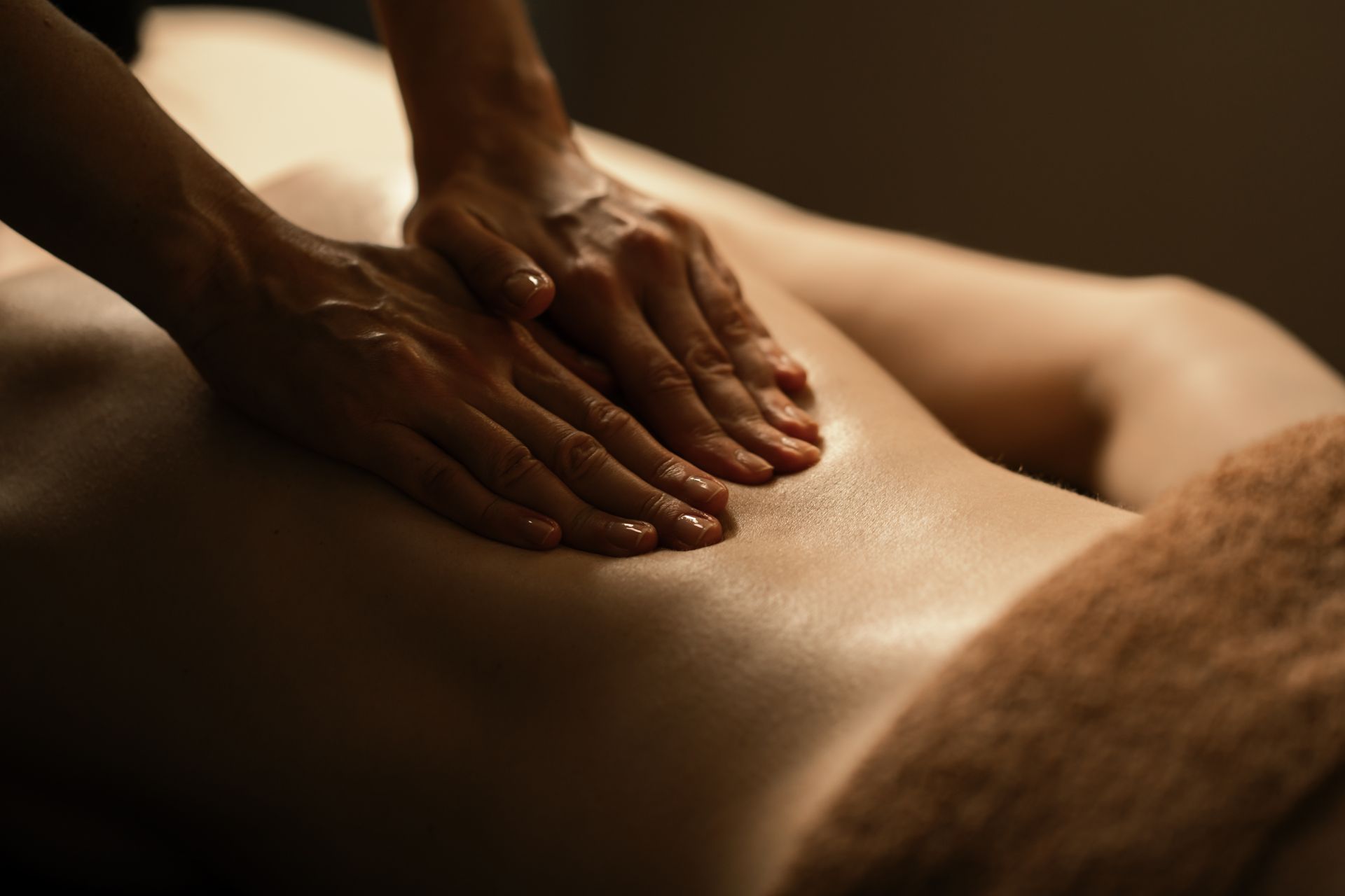 Hands massaging a person's back; massage table and towel in soft light.