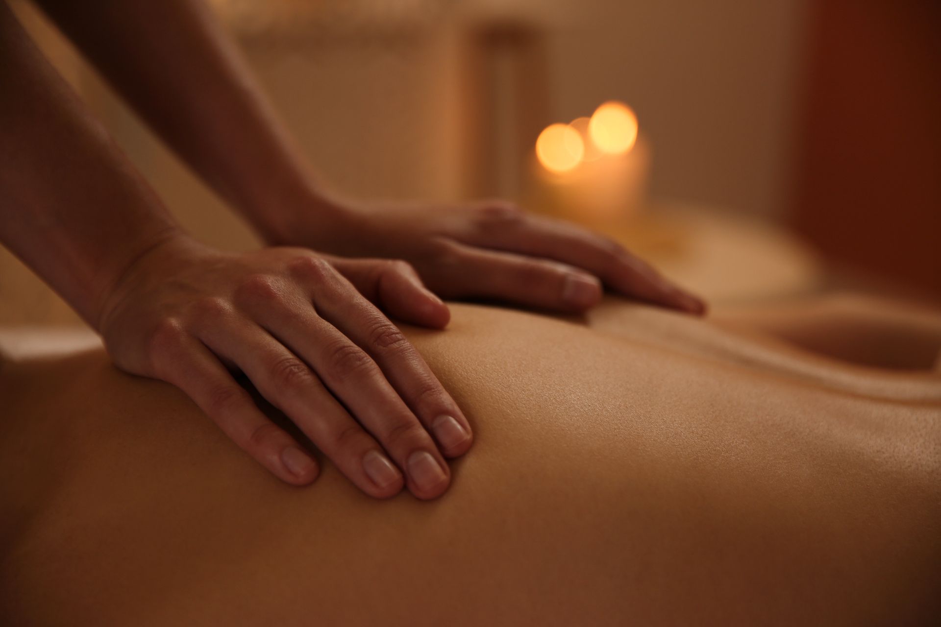 Hands giving back massage, soft skin, candlelit setting.