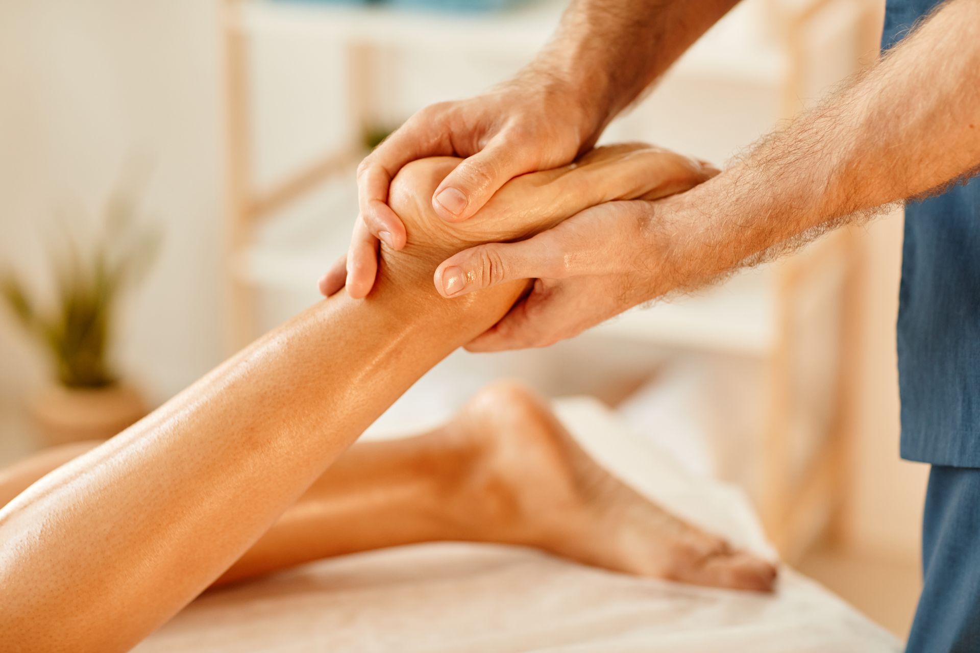 Hands massaging a person's foot and ankle on a massage table.