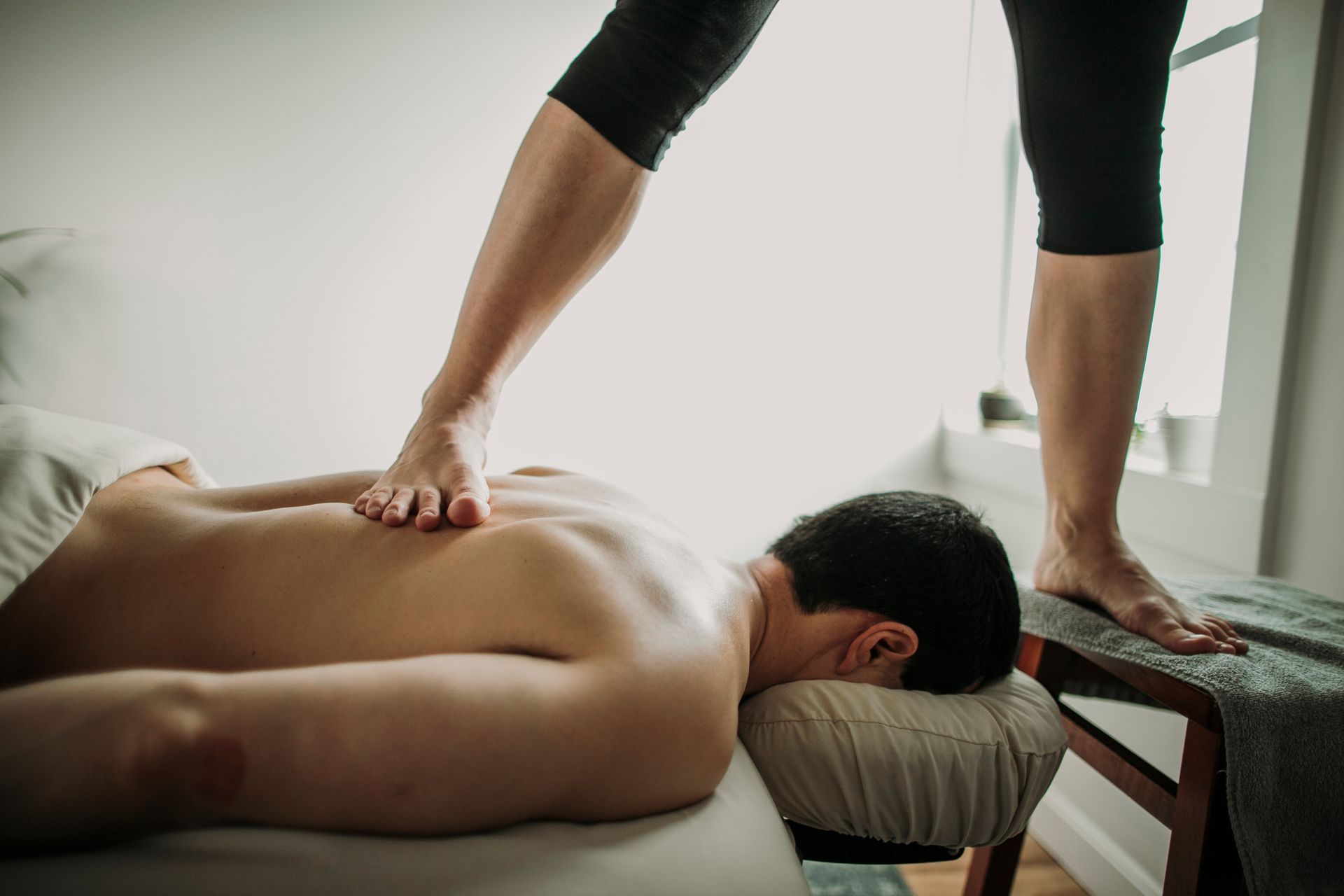 Person receiving back massage with foot pressure; white room.