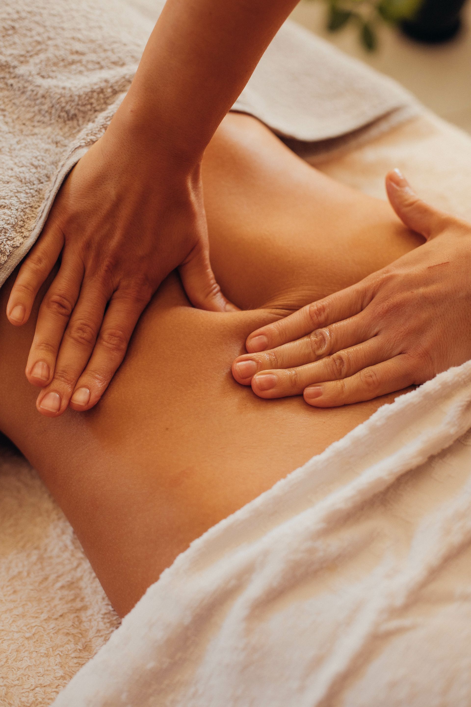 Hands massaging a person's lower back, covered with a white towel.