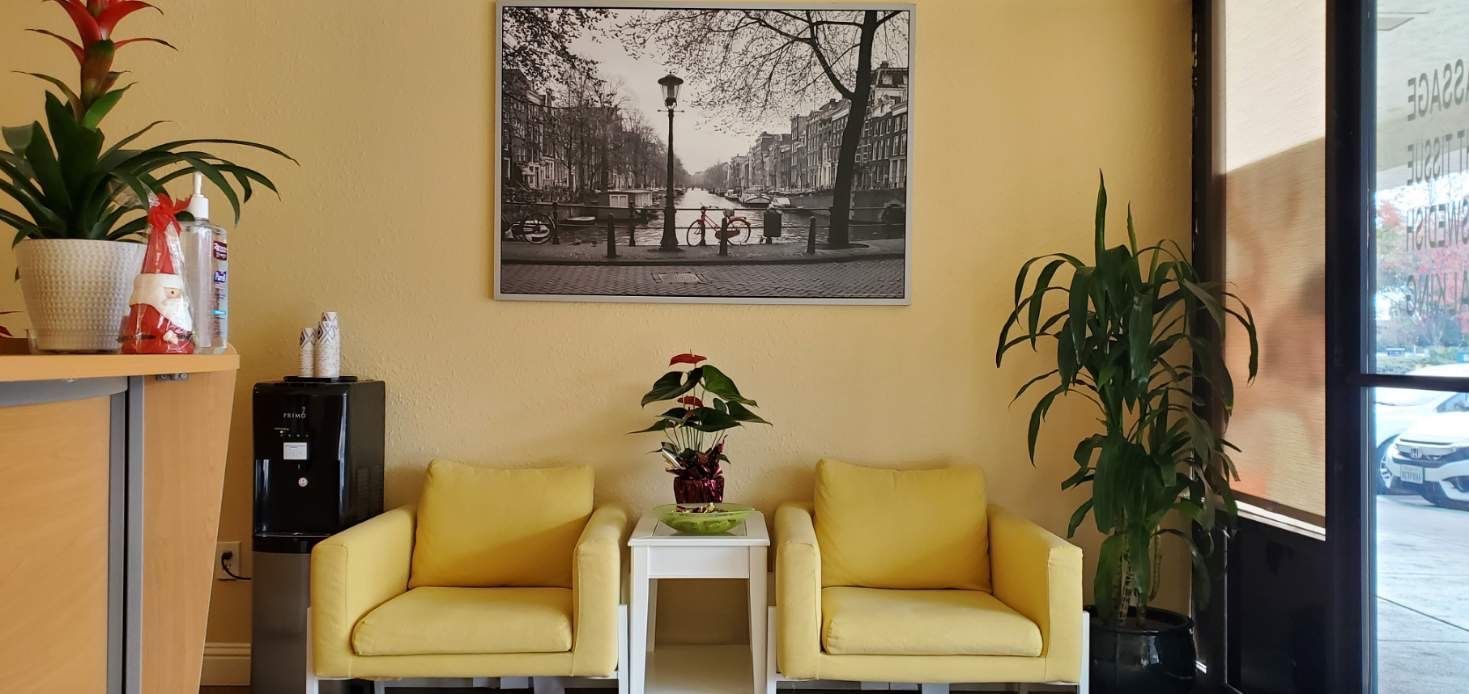 A waiting room with yellow chairs, plants, and a black and white picture above the chairs.