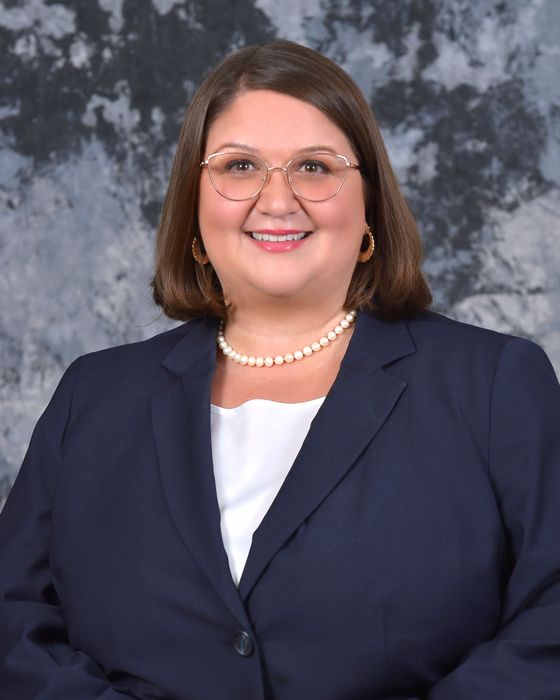 A woman wearing glasses and a pearl necklace is smiling for the camera.