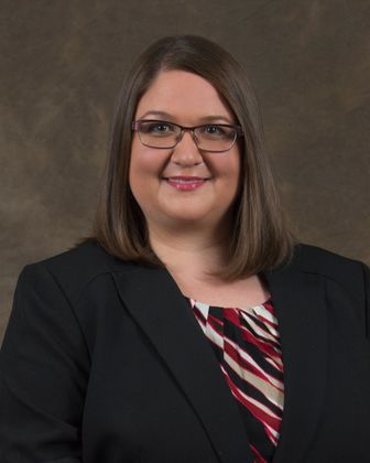 A woman wearing glasses and a black jacket is smiling for the camera.