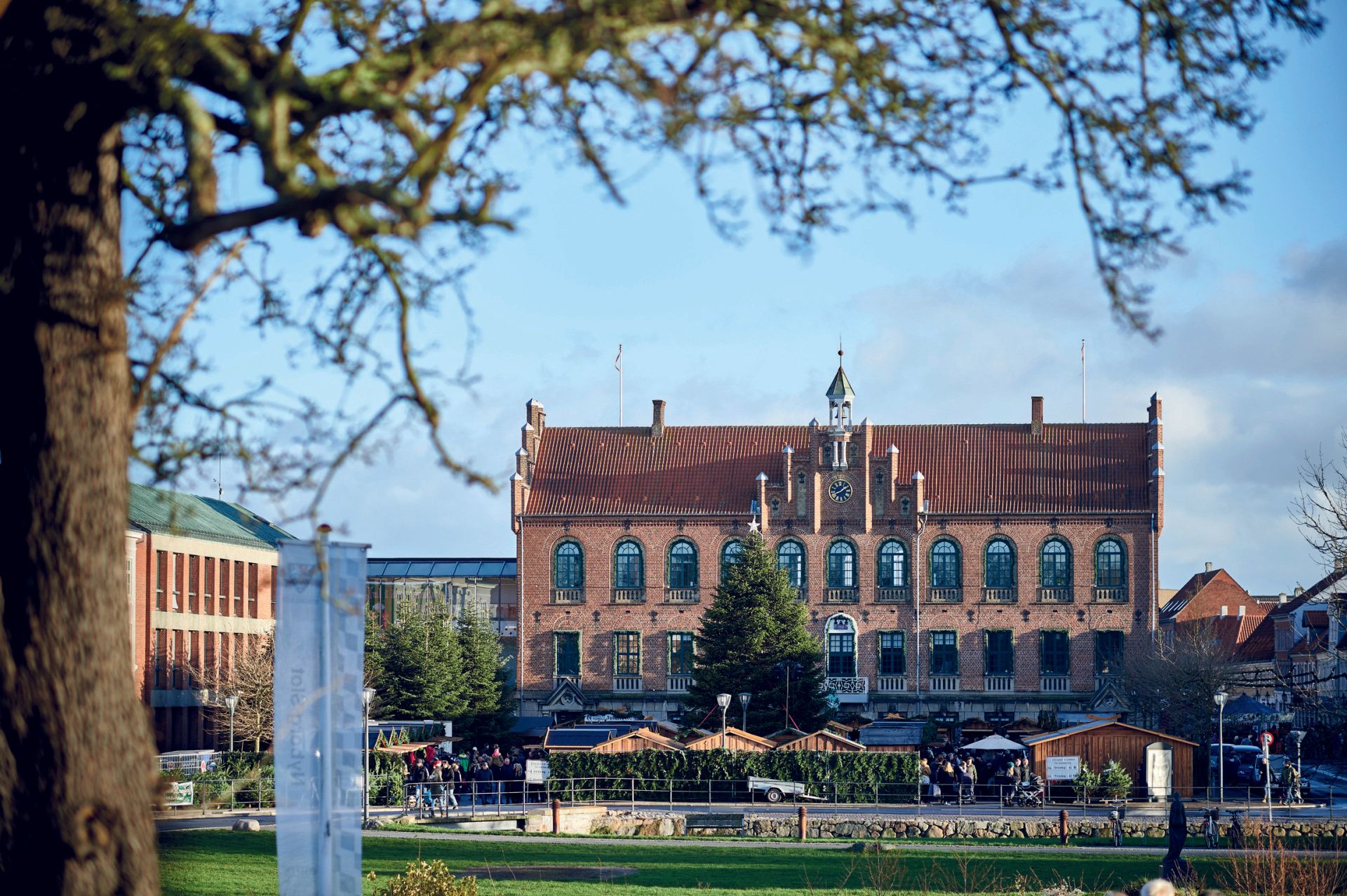 En stor bygning med rødt tegltag er omgivet af træer i en park.
