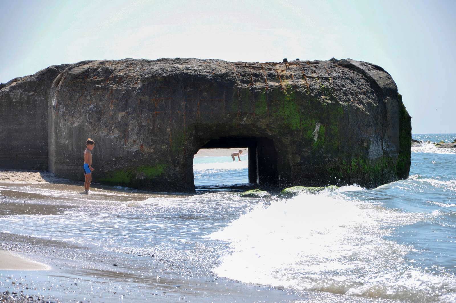 En mand står på en strand ved siden af ​​en stor sten i vandet.