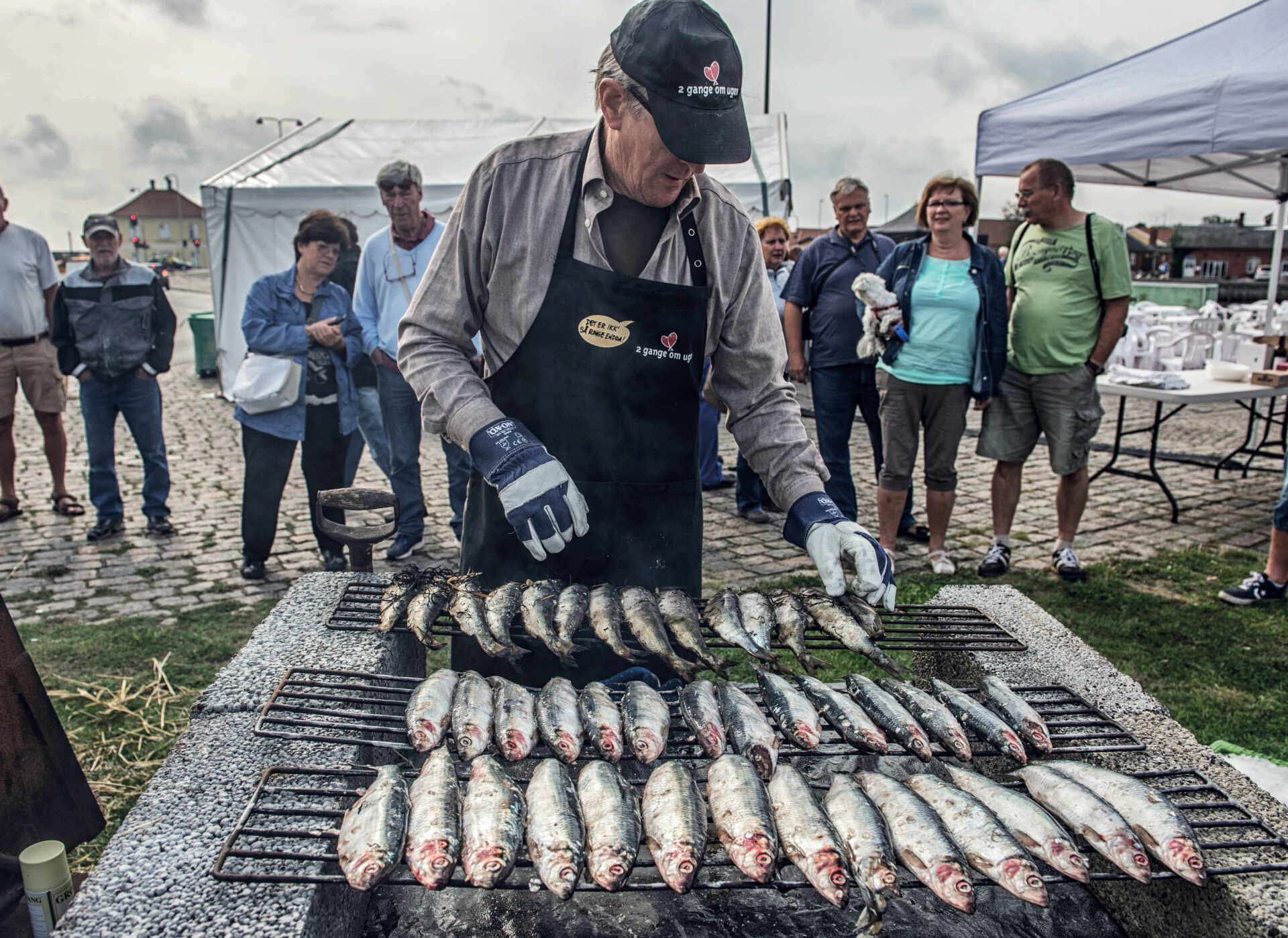 En mand tilbereder fisk på en grill foran en menneskemængde.