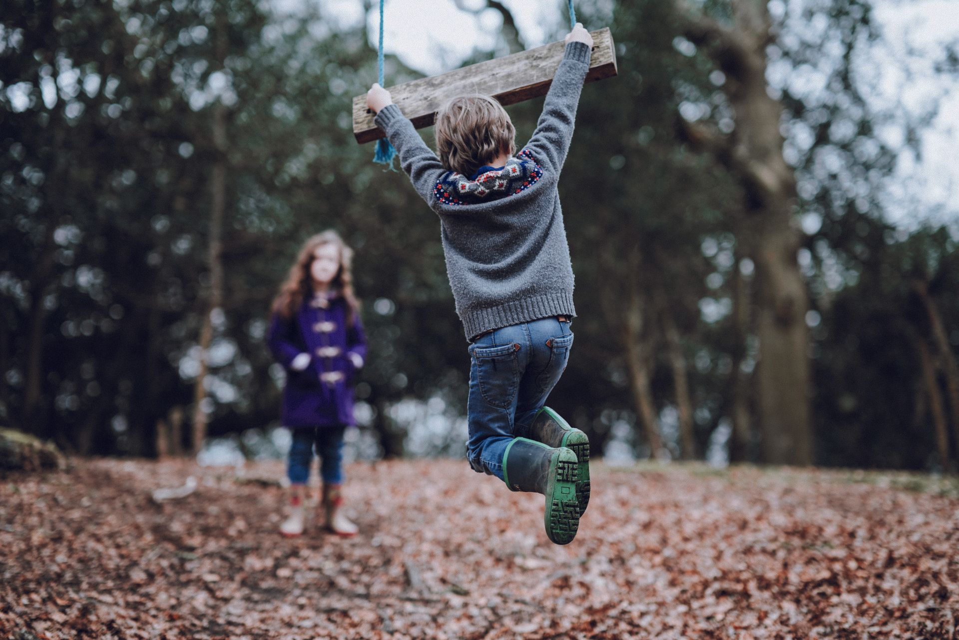 En dreng og en pige leger på en gynge i skoven.